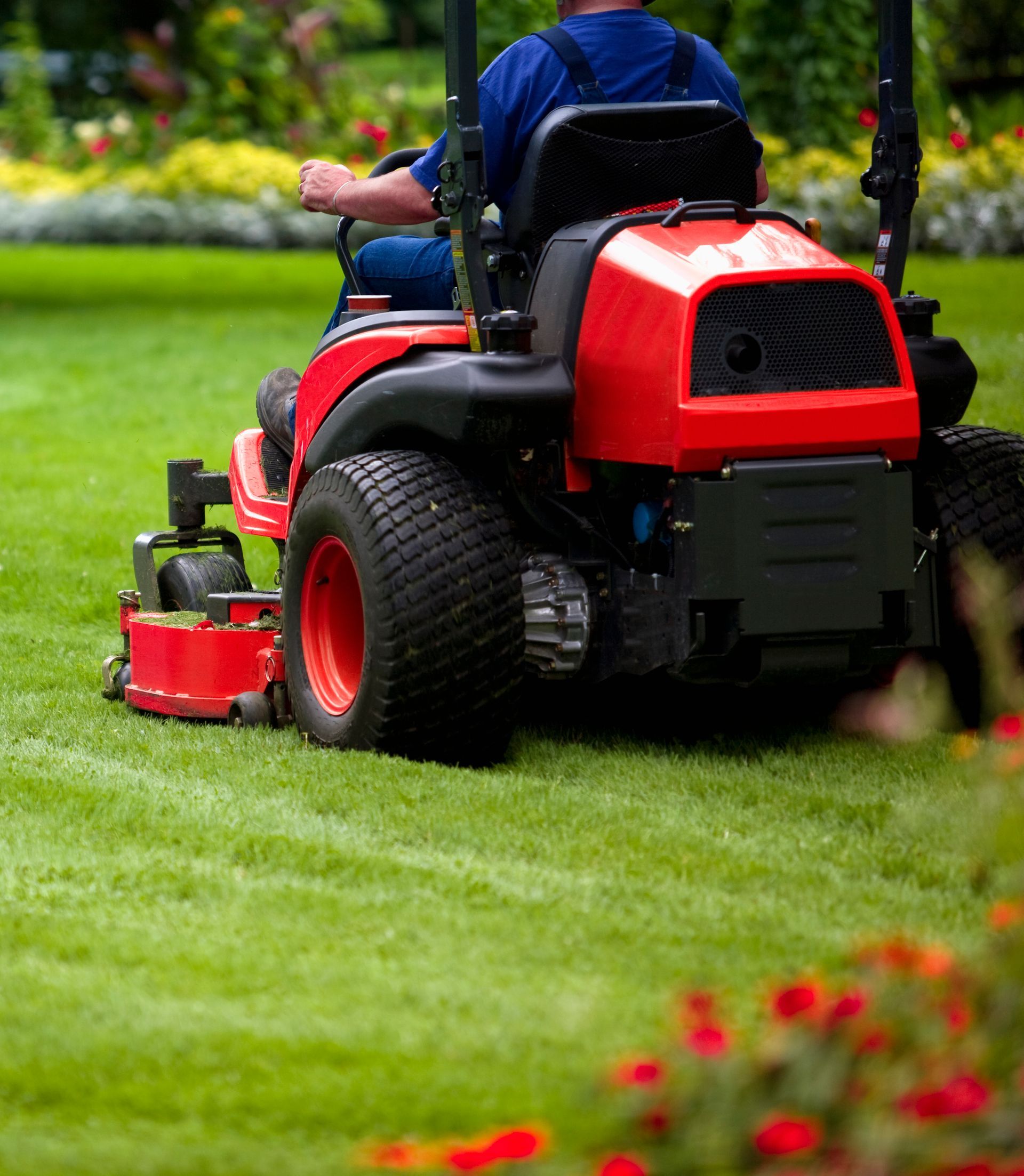A man is riding a red lawn mower on a lush green lawn.