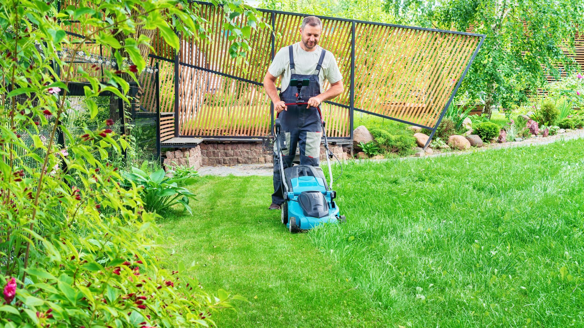 A man is mowing a lush green lawn with a light blue lawn mower.
