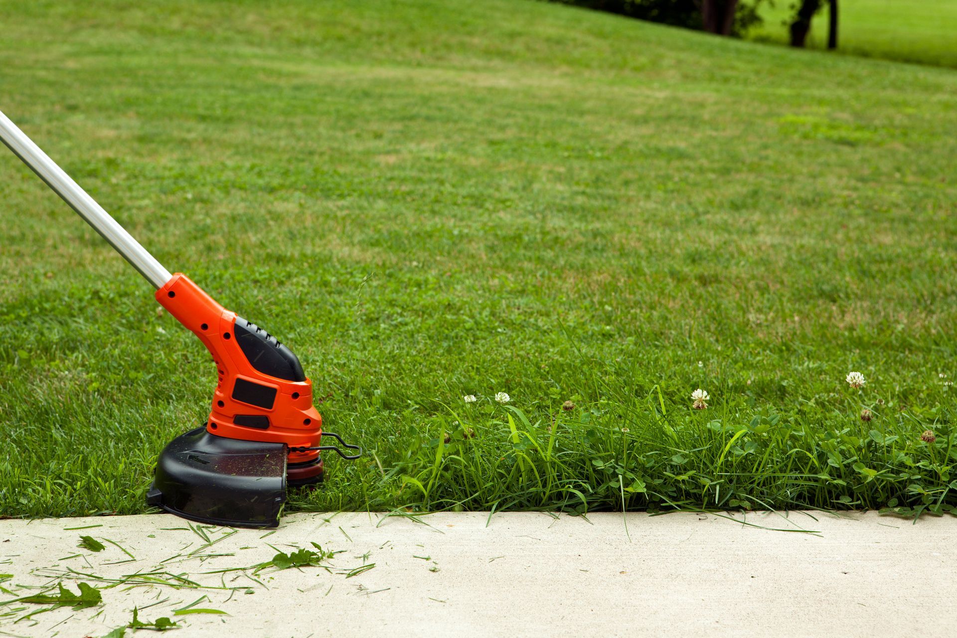 A lawn mower is cutting grass on the sidewalk.