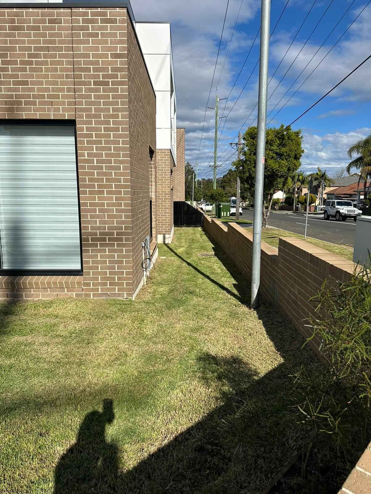 A shadow of a person is cast on the grass in front of a brick building.