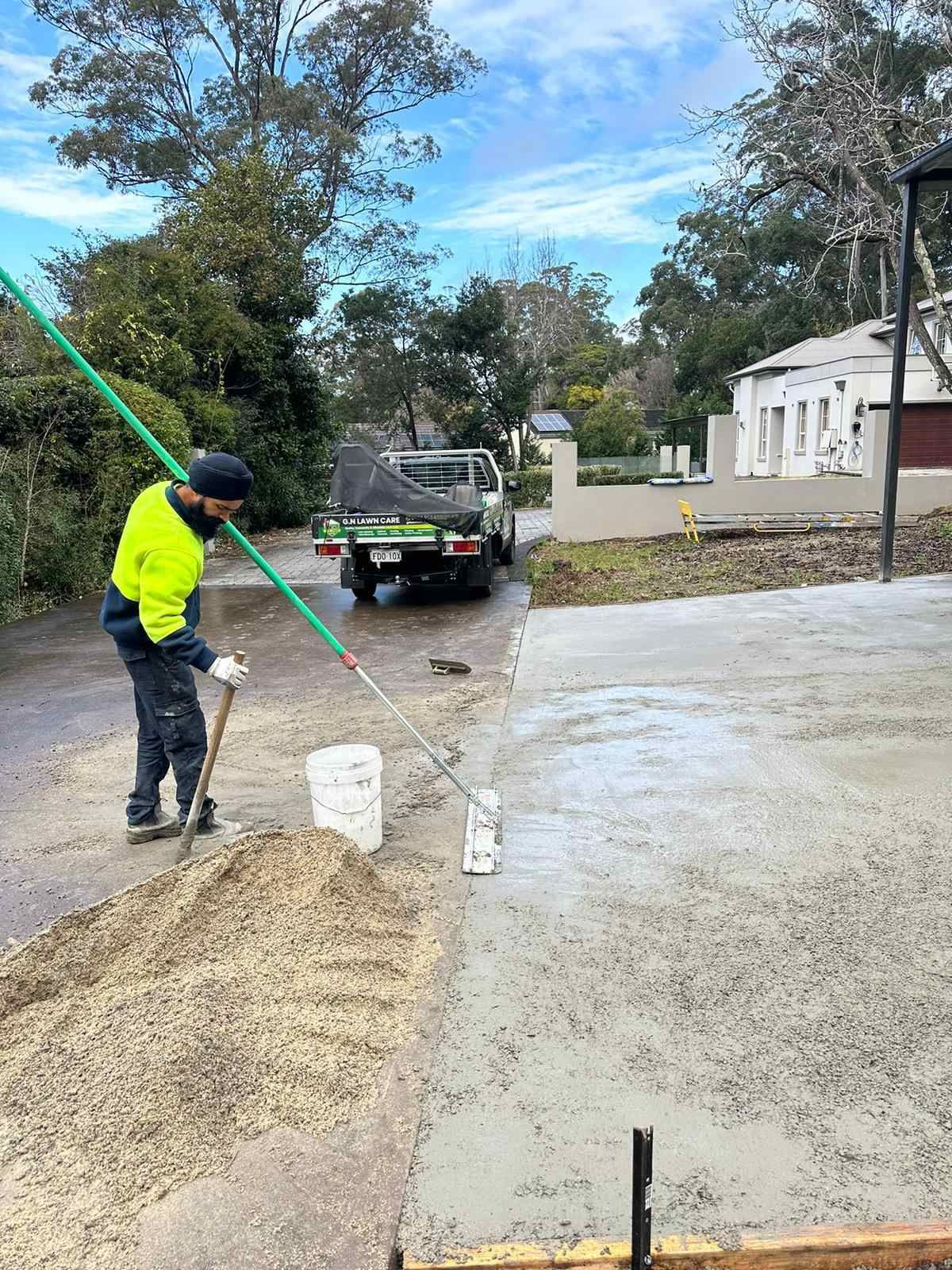 A man is spreading concrete on the side of a road.