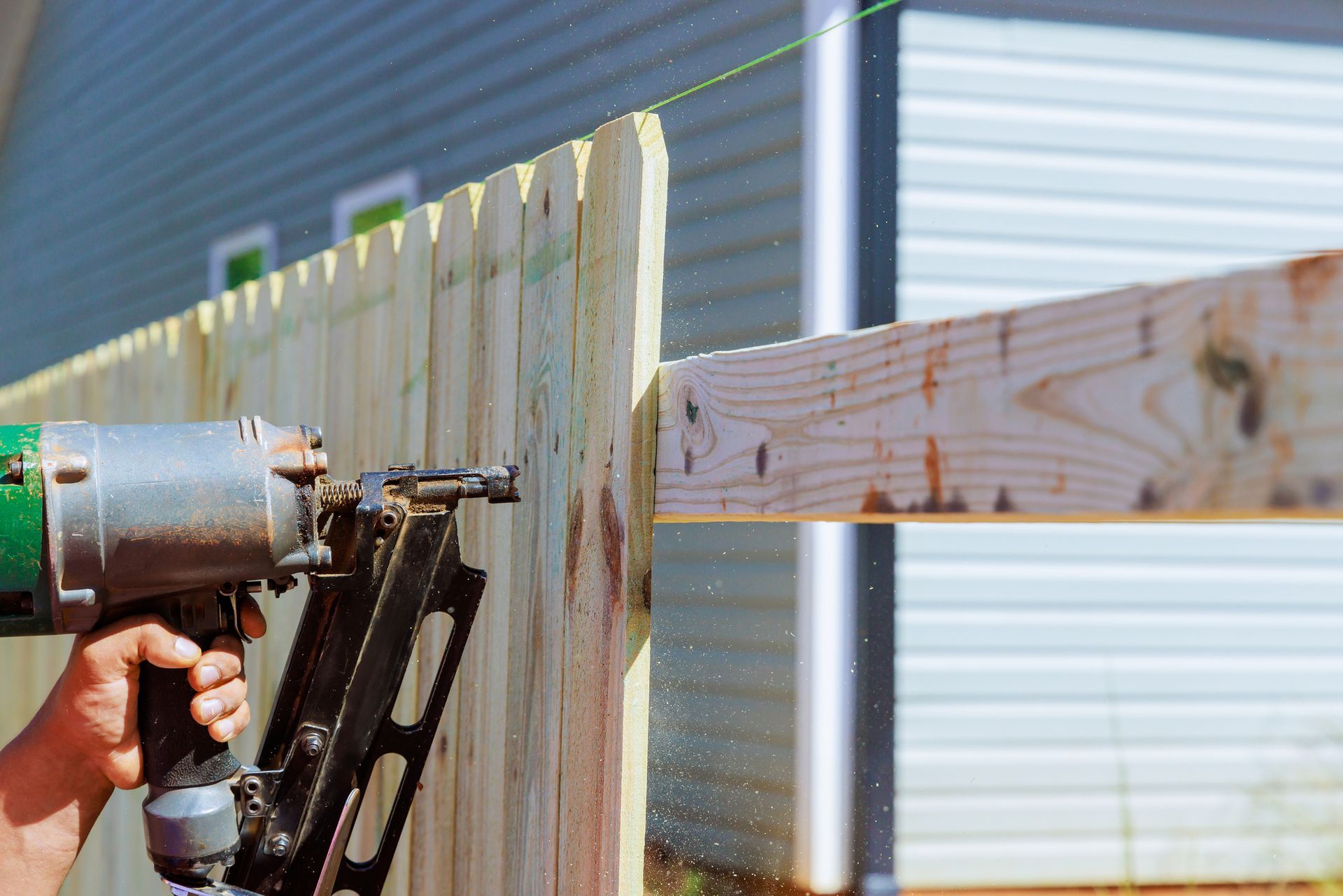 A person is using a metal drill to install a wooden fence.