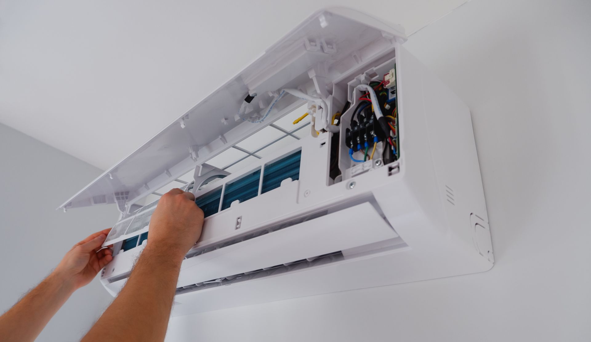 Hands opening a wall-mounted AC unit's front panel to access the filter for service