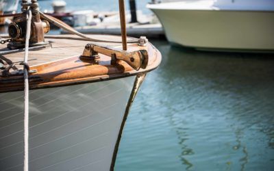 Close-up of a wooden sailboat bow moored beside calm blue-green water and another boat.
