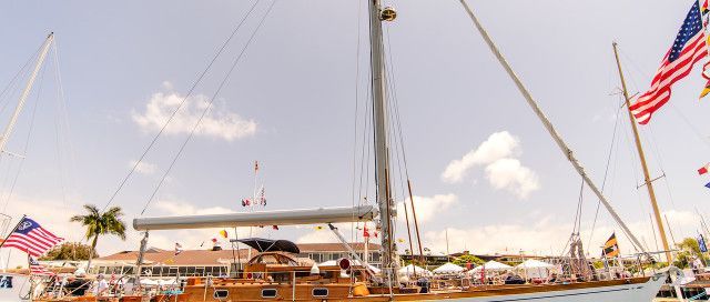 Large sailboat docked at a marina with people on deck and a waving American flag at sunset