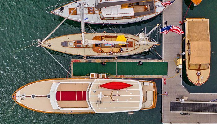 Top-down view of three docked sailboats and a tan motorboat beside a wooden pier.