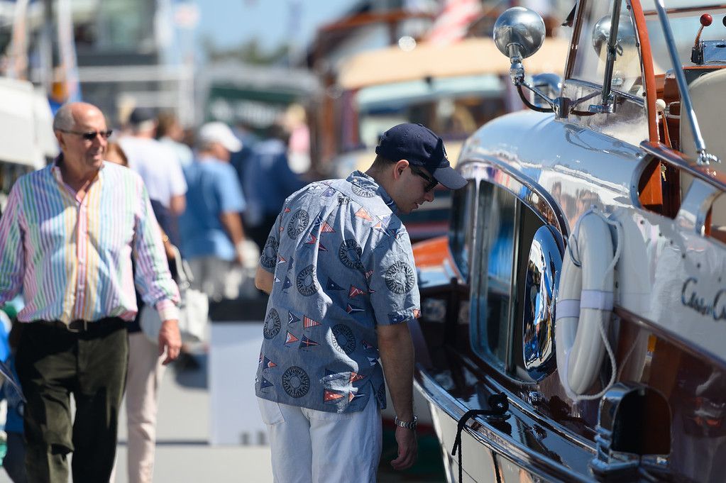 People browsing a classic car at an outdoor street event, with a shiny vintage vehicle in the foreground.
