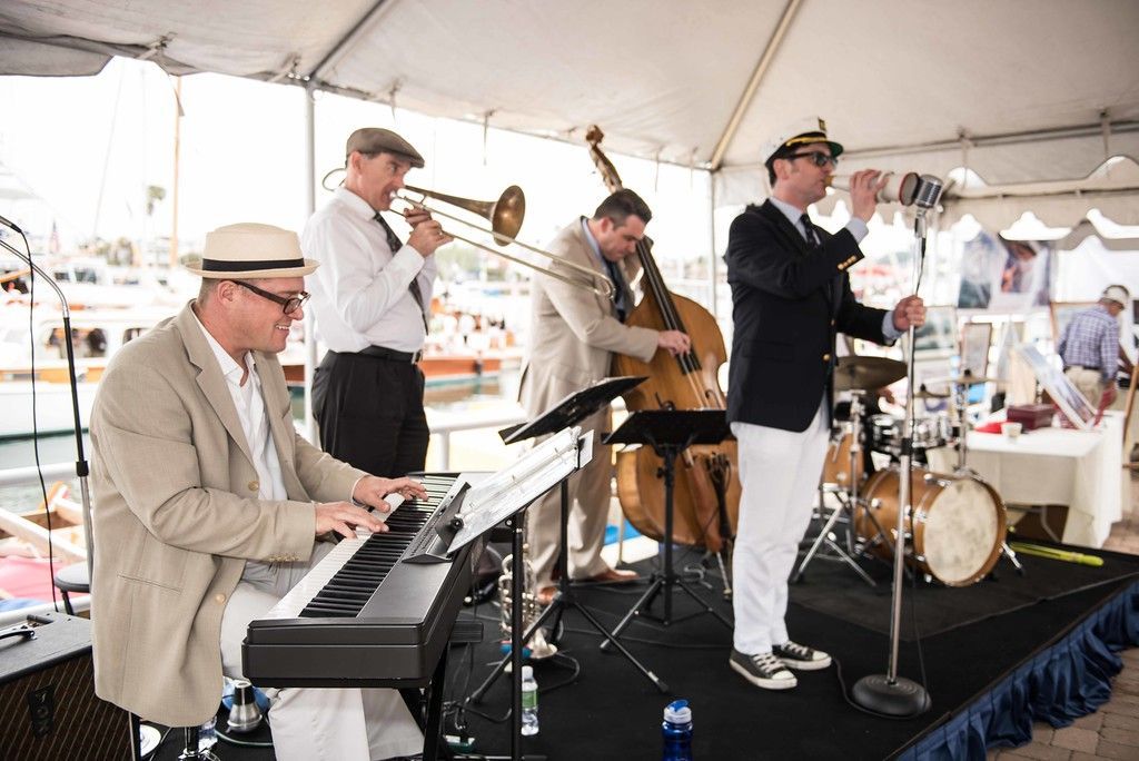 Jazz band performing under a white tent, with piano, trumpet, bass, and drums on stage.