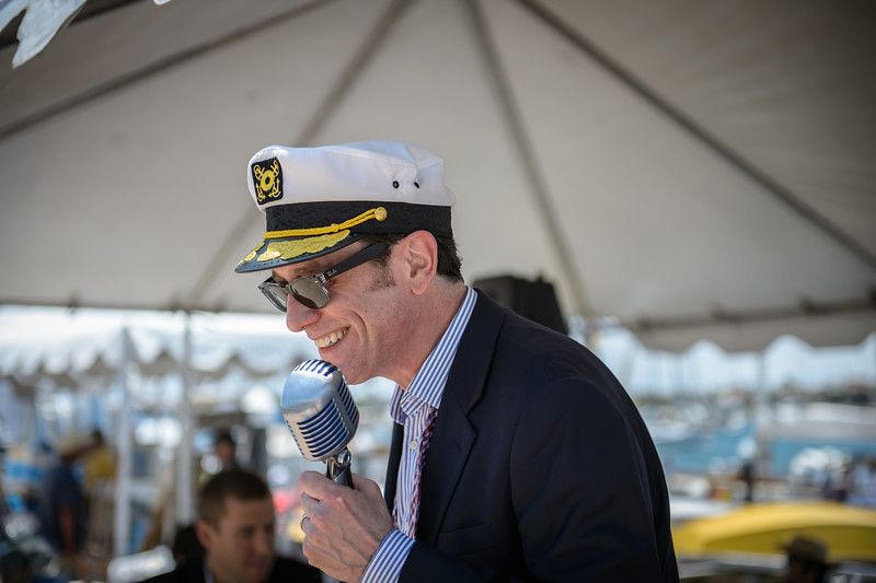 Man in a white captain’s hat speaking into a microphone at an outdoor event