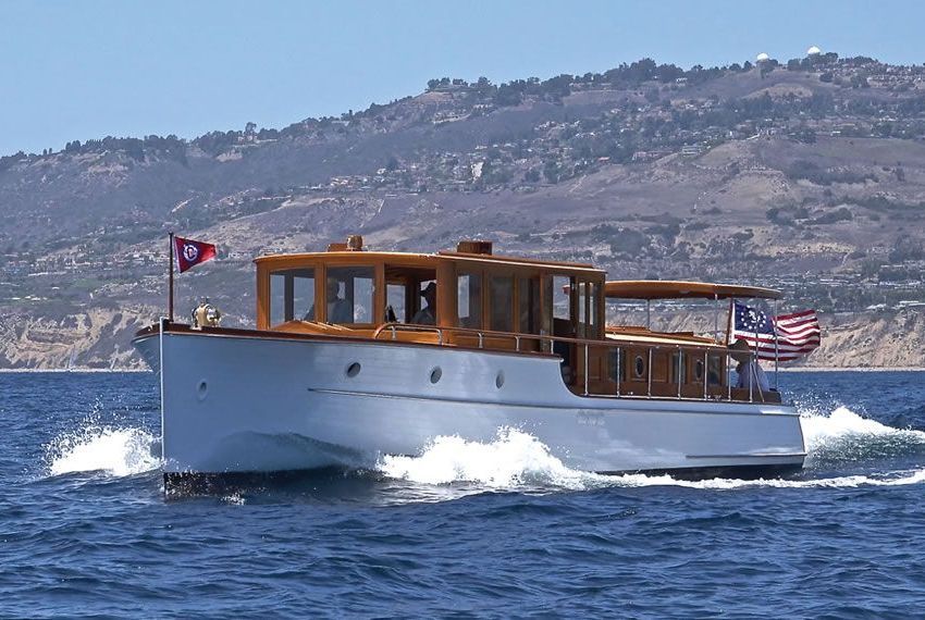White wooden motorboat cruising on blue water with a rocky coastline in the background