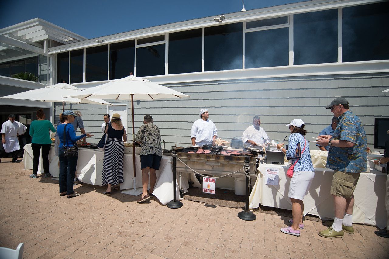 People standing at a beachside buffet table outside a modern building, serving food under umbrellas