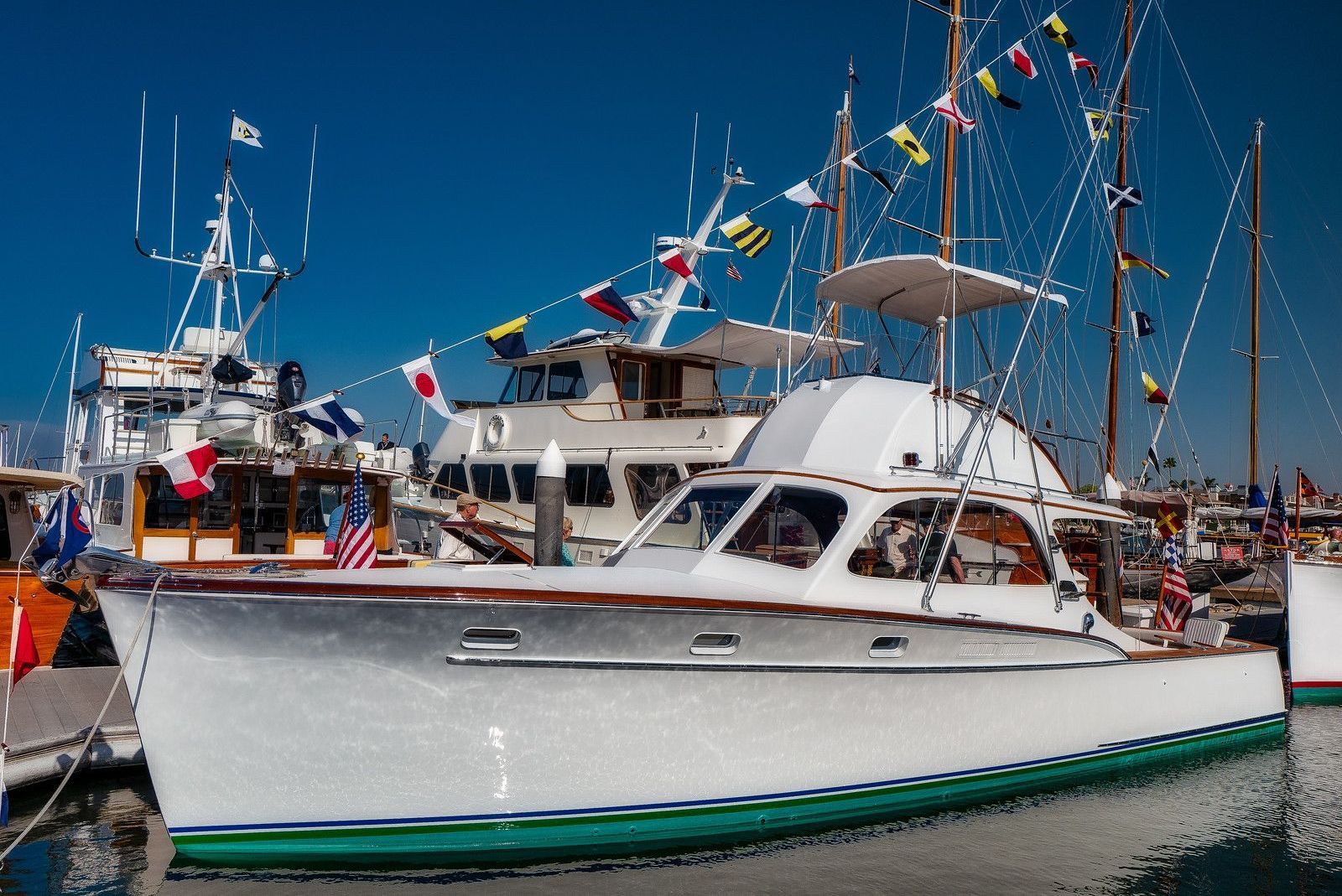 White sailboat docked in a marina with other boats and colorful flags under a bright blue sky