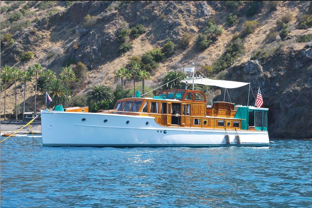 Wooden tour boat with white hull floating on blue water near a rocky shoreline.