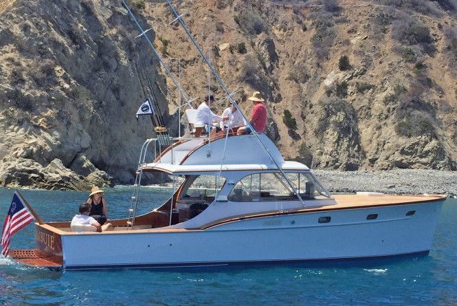 White motor yacht with people aboard cruising on blue water near rocky cliffs