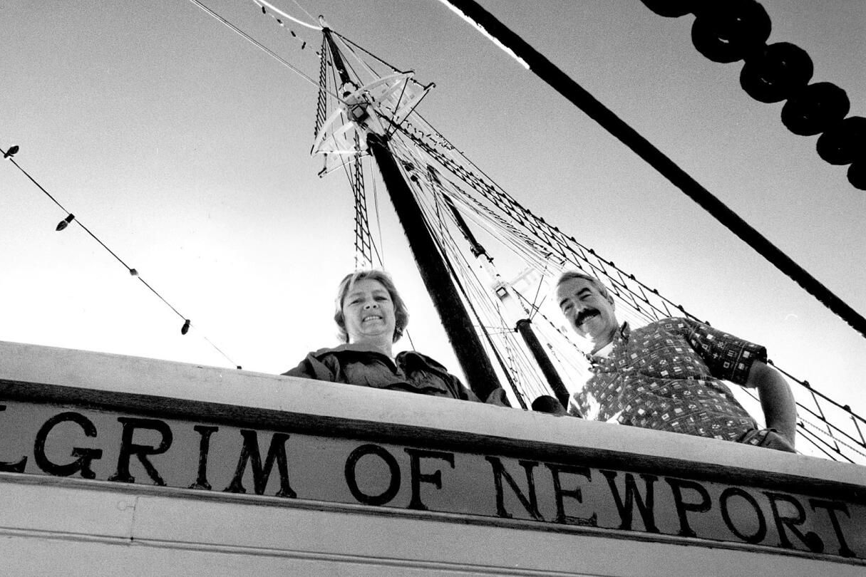 Two people on a boat deck beneath rigging, with “Pilgrim of Newport” visible on the bow.