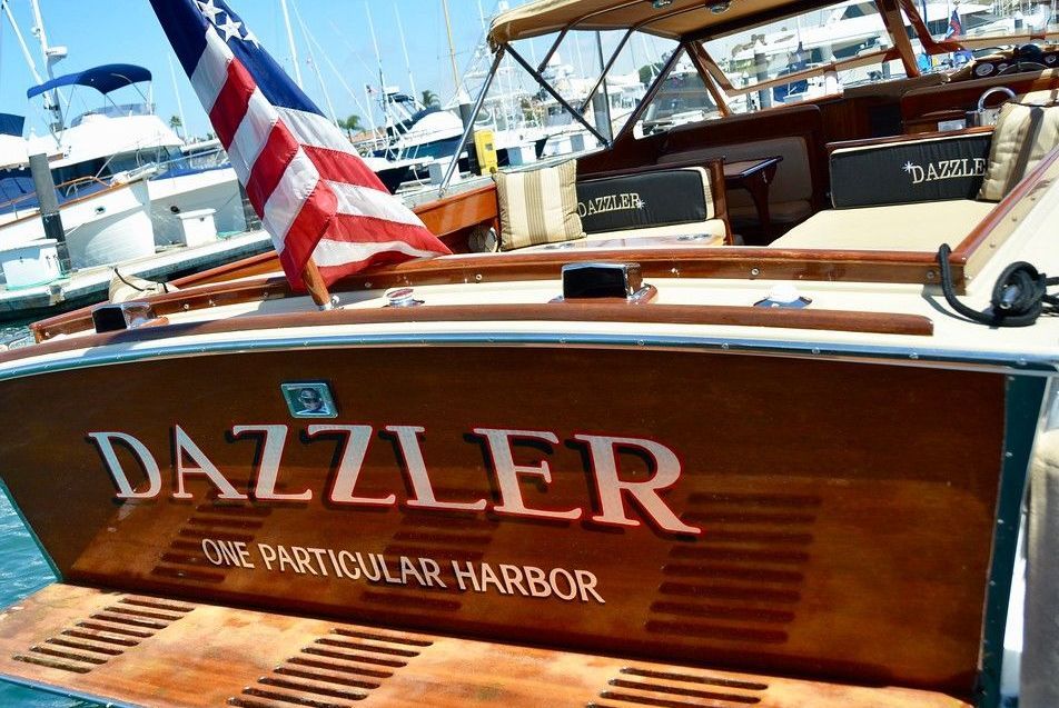 Wooden boat named “DAZZLER” with an American flag at a harbor marina