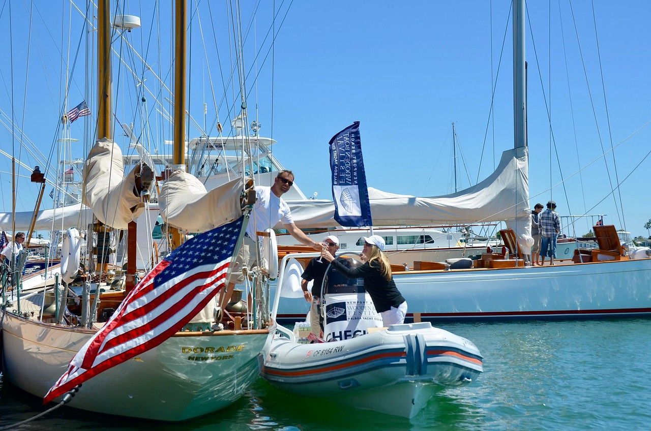Small inflatable boat with people beside sailboats in a sunny marina, U.S. flag in foreground