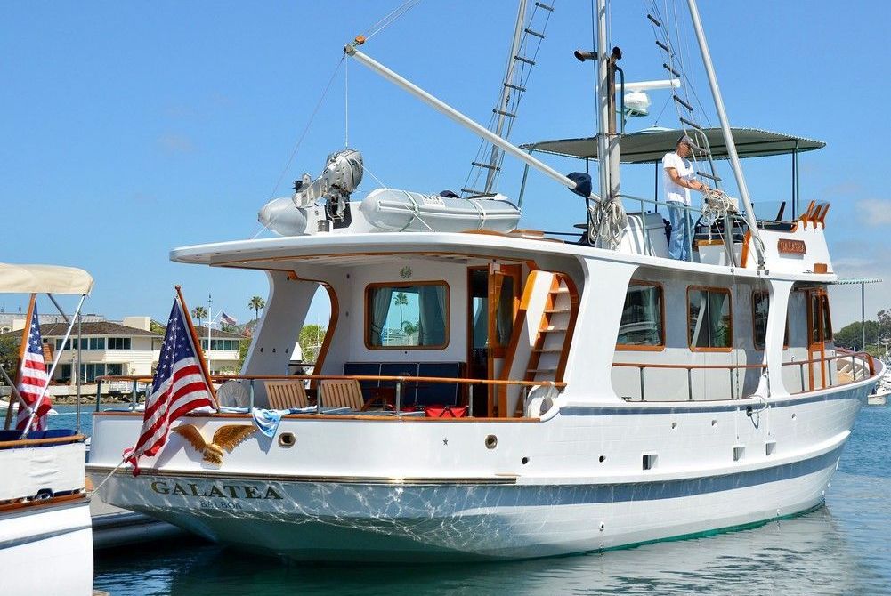 White motor yacht docked on calm water, with U.S. flags and people on deck under a blue sky