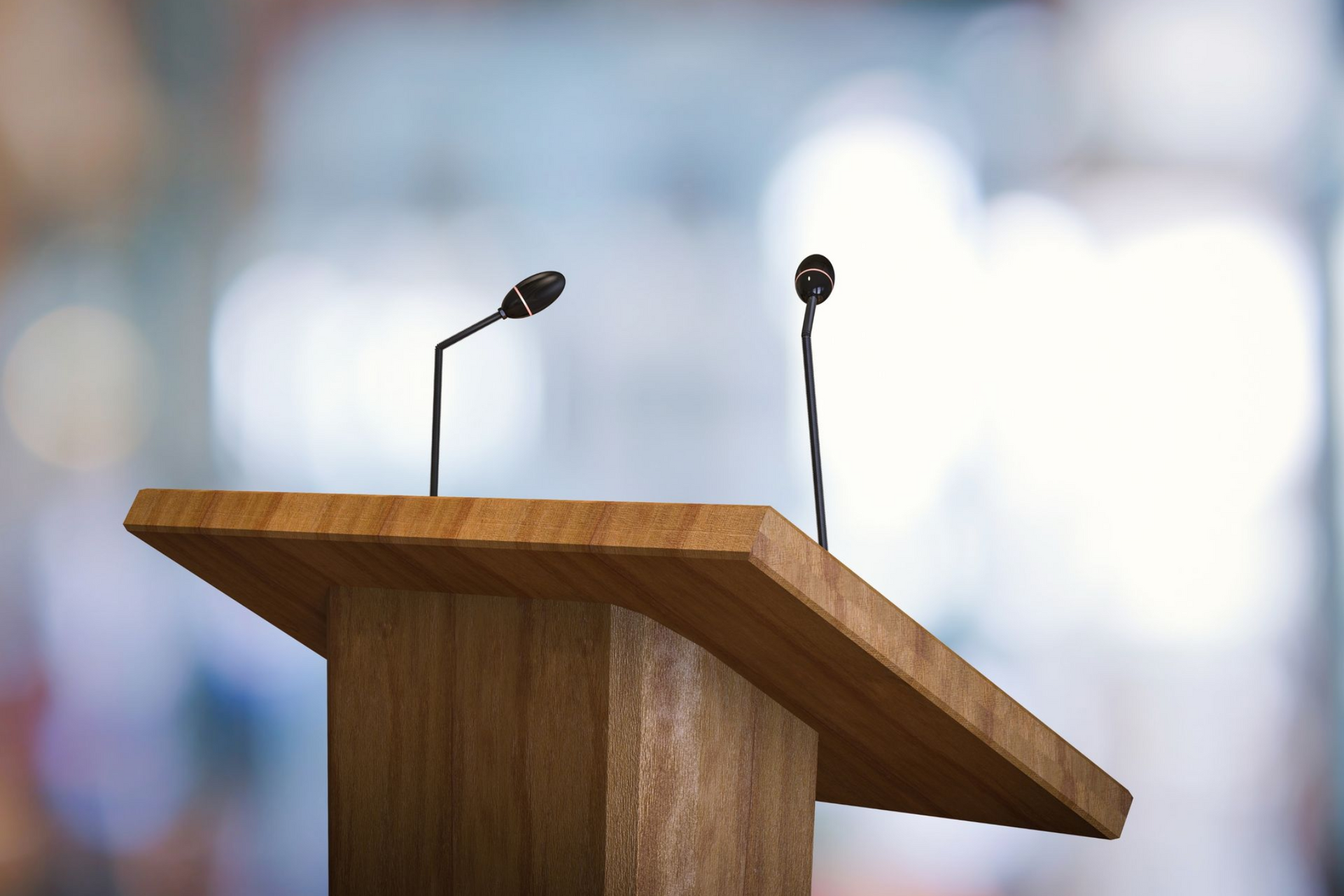 Wooden podium with two microphones against a blurred background