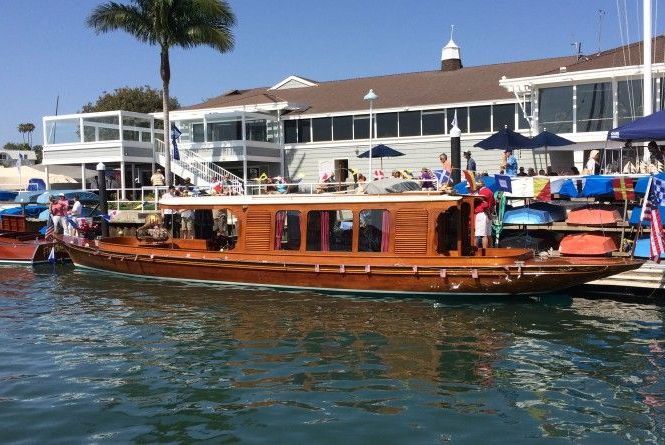 Wooden tour boat docked on calm water near a marina and waterfront buildings