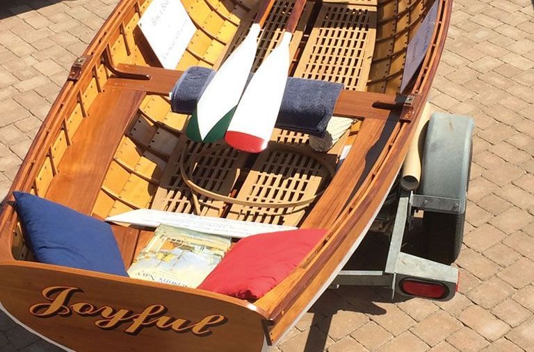 Wooden rowboat on brick pavement with blue and red cushions and oars inside.
