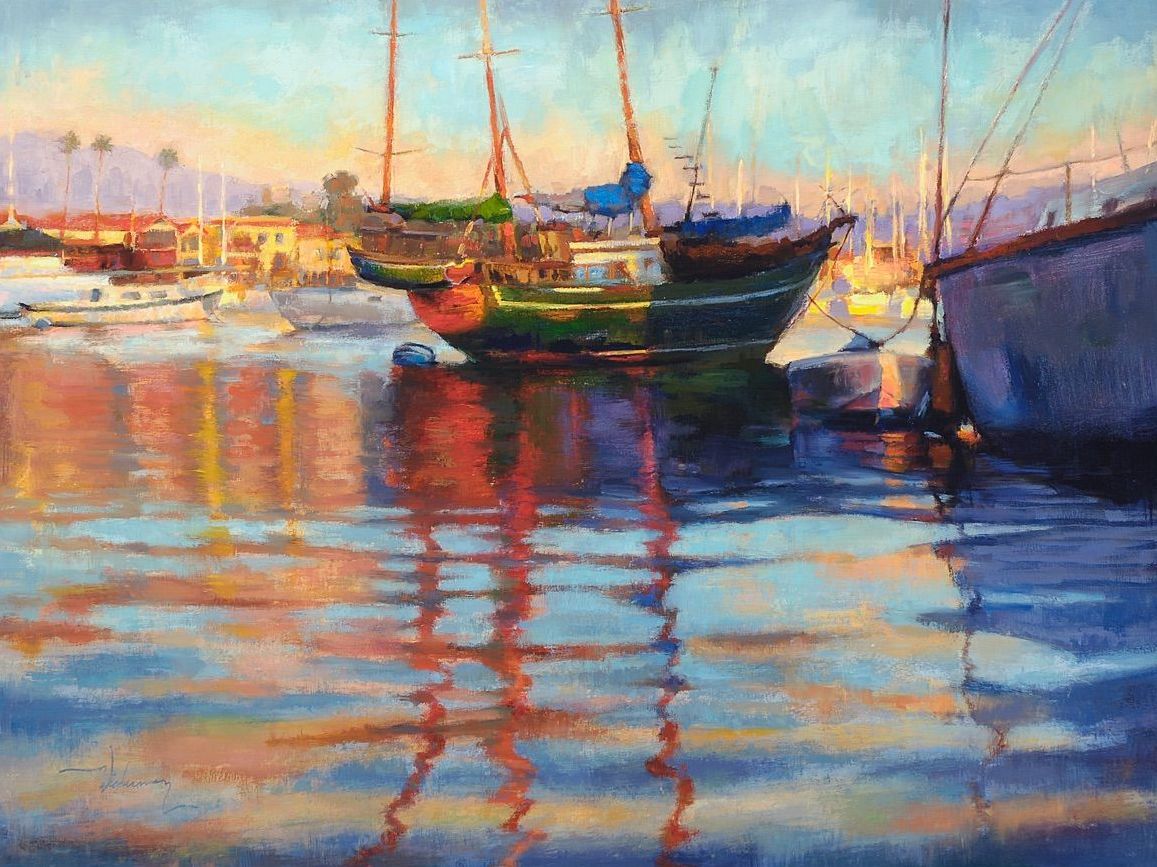 Colorful sailboats reflected in calm water at sunset by a harbor.