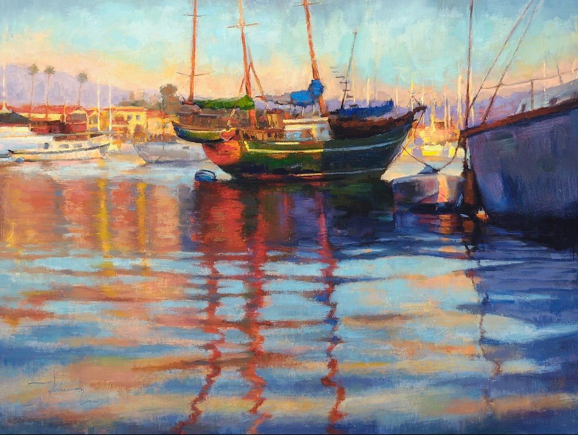 Colorful sailboats reflected on calm harbor water at sunset, with a docked boat at right.