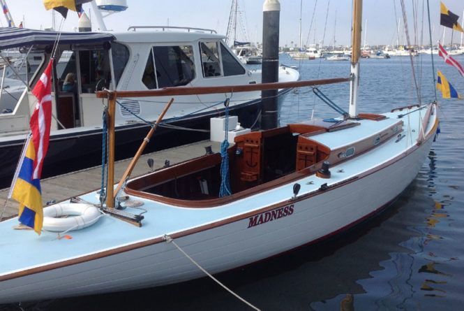 White sailboat docked in a harbor, with blue trim and colorful flags, beside another boat