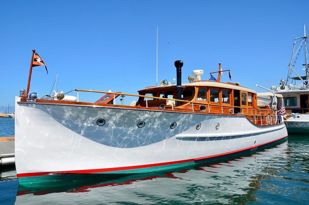 Wooden motor yacht with white hull and orange cabin docked on calm blue water under clear sky