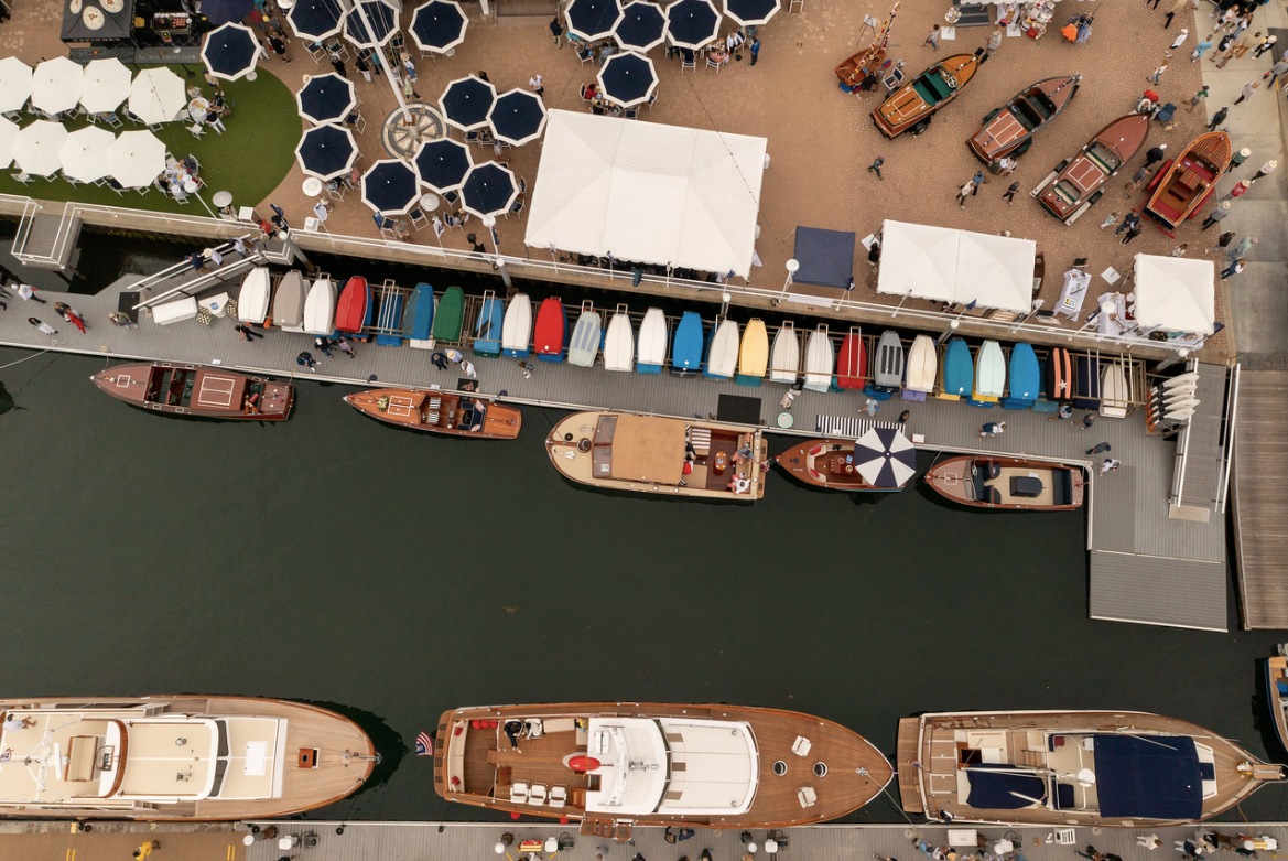 Aerial view of a marina with docked boats, colorful kayaks, and white tents along the water's edge