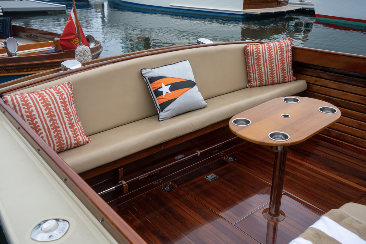 Boat deck seating area with beige cushions, patterned pillows, and a small wooden table beside the water.