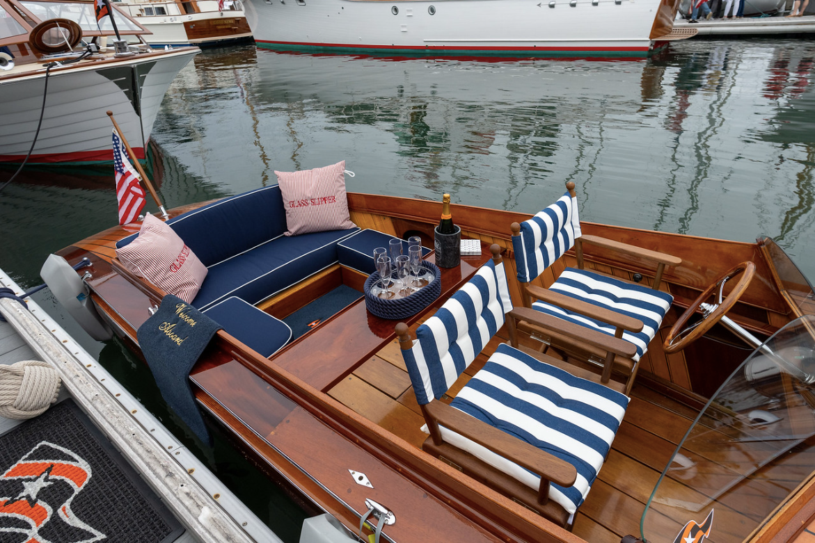 Wooden boat with navy and white striped cushions docked on calm water, with neighboring boats reflected nearby