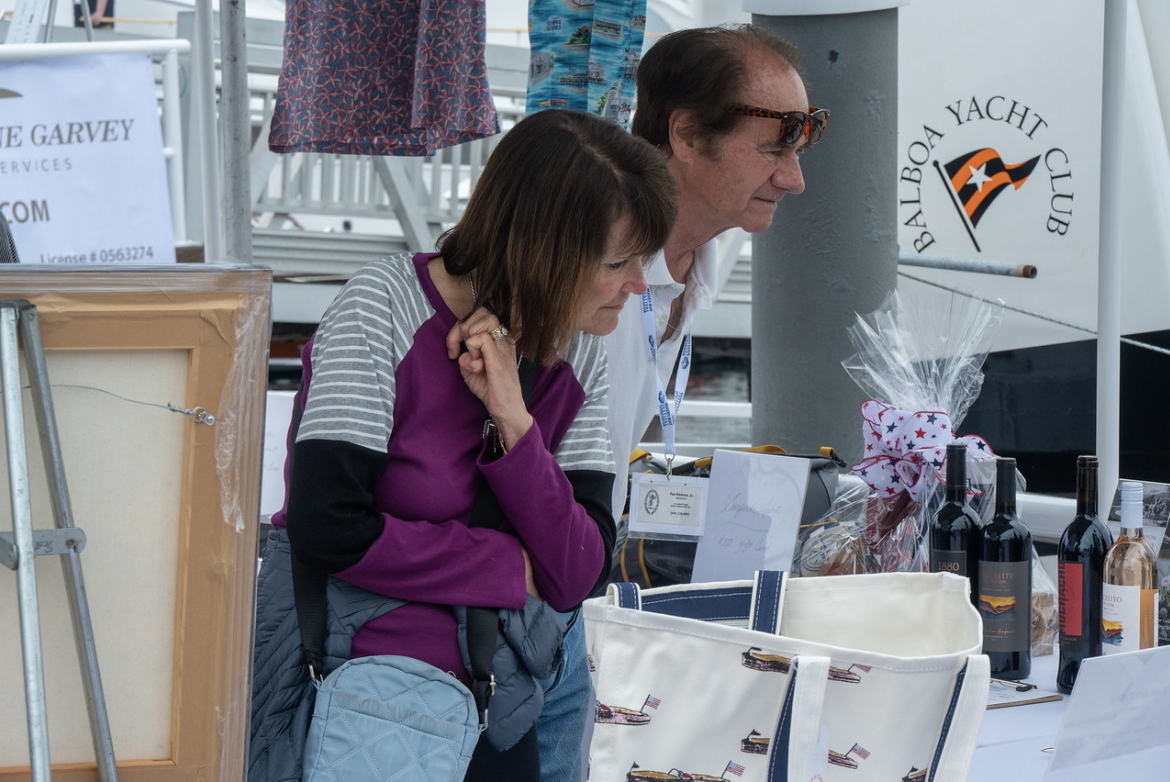 Two people at an outdoor market stall with bottles, gifts, and wrapped items on display