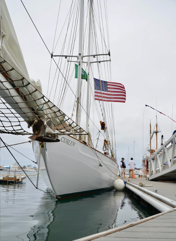 Sailboat docked in a harbor with a U.S. flag and people on the pier