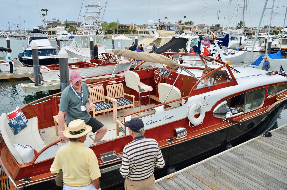 People boarding a red-and-white motorboat at a marina, with other boats in the background