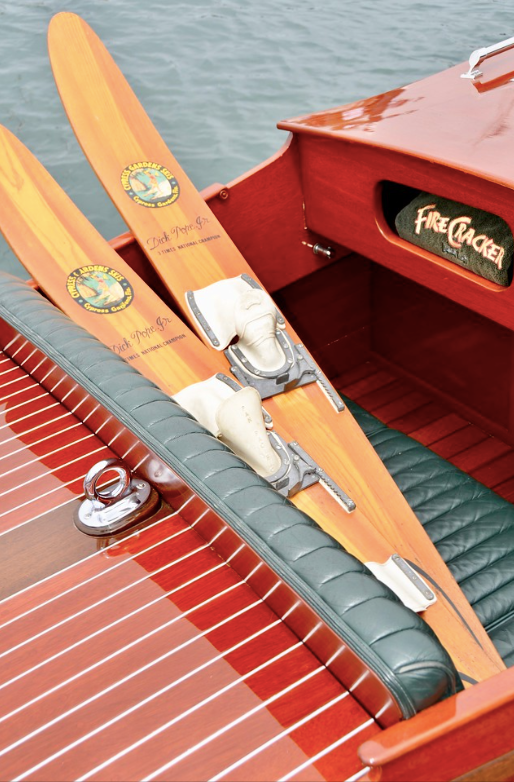 Two wooden skis with bindings resting in a red wooden boat beside a lake