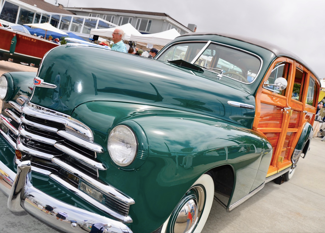 Green vintage woody station wagon with chrome grille and wooden side panels, parked outdoors at a car show