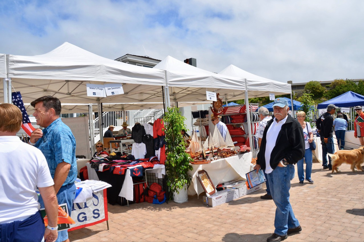 Outdoor market stalls under white tents with people browsing handmade goods on a sunny day