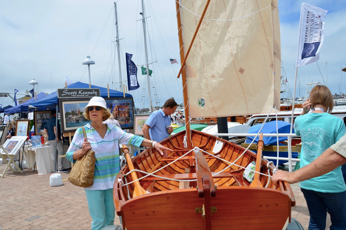 Wooden sailboat at a marina with two people nearby under a bright sky