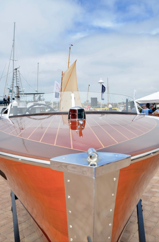 Front view of a classic sailboat with a wooden deck and red hull docked at a marina