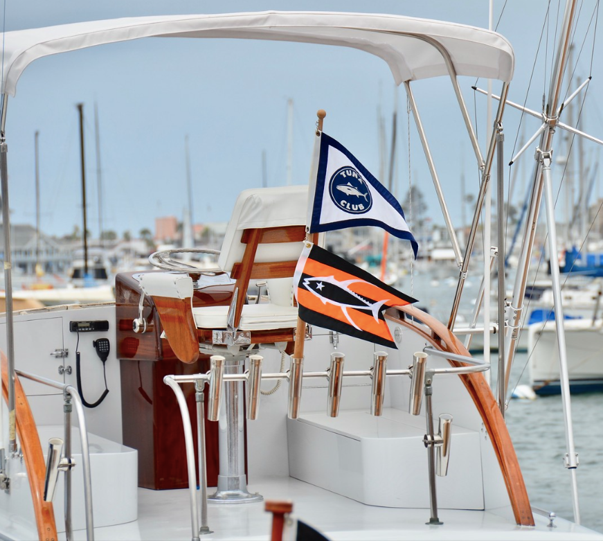 Sailboat deck with white canopy, wooden helm, and two nautical flags in a marina