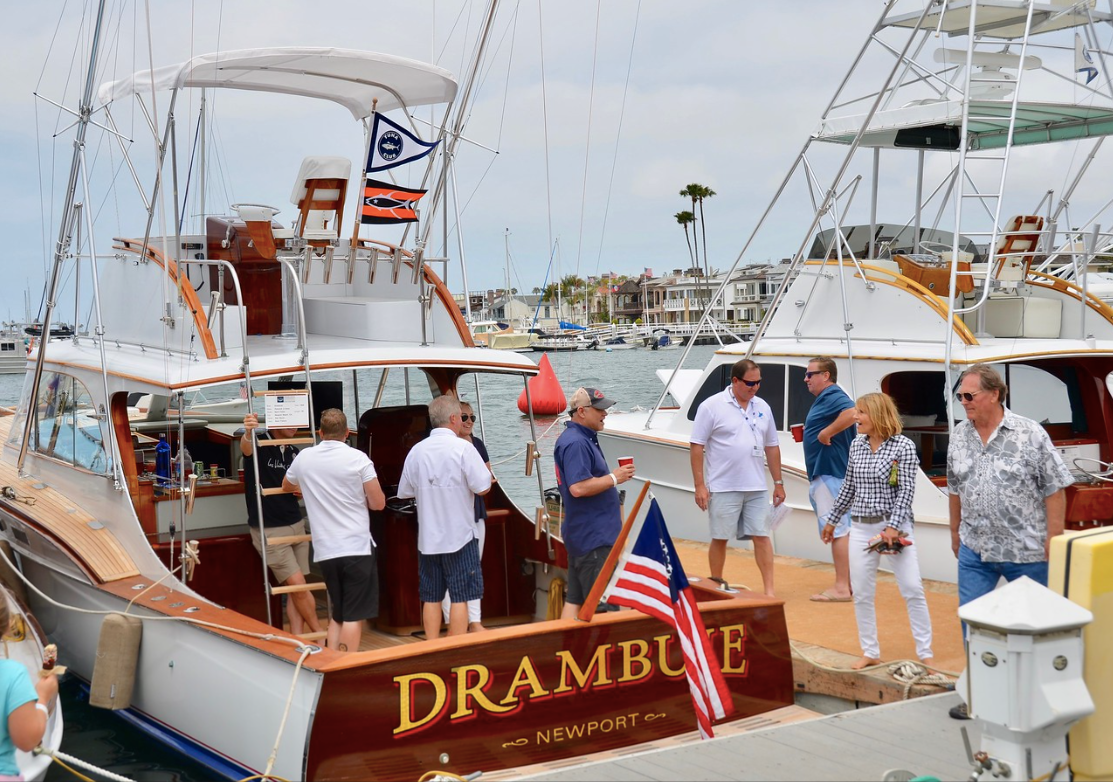 Luxury yachts docked at a marina, with people boarding the stern of the boat “DRAMBUIE.”