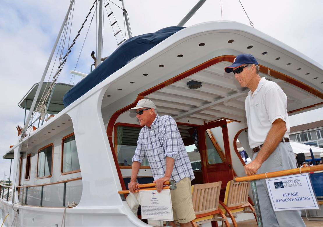 Two men on a boat deck, looking up at the mast under a white canopy.