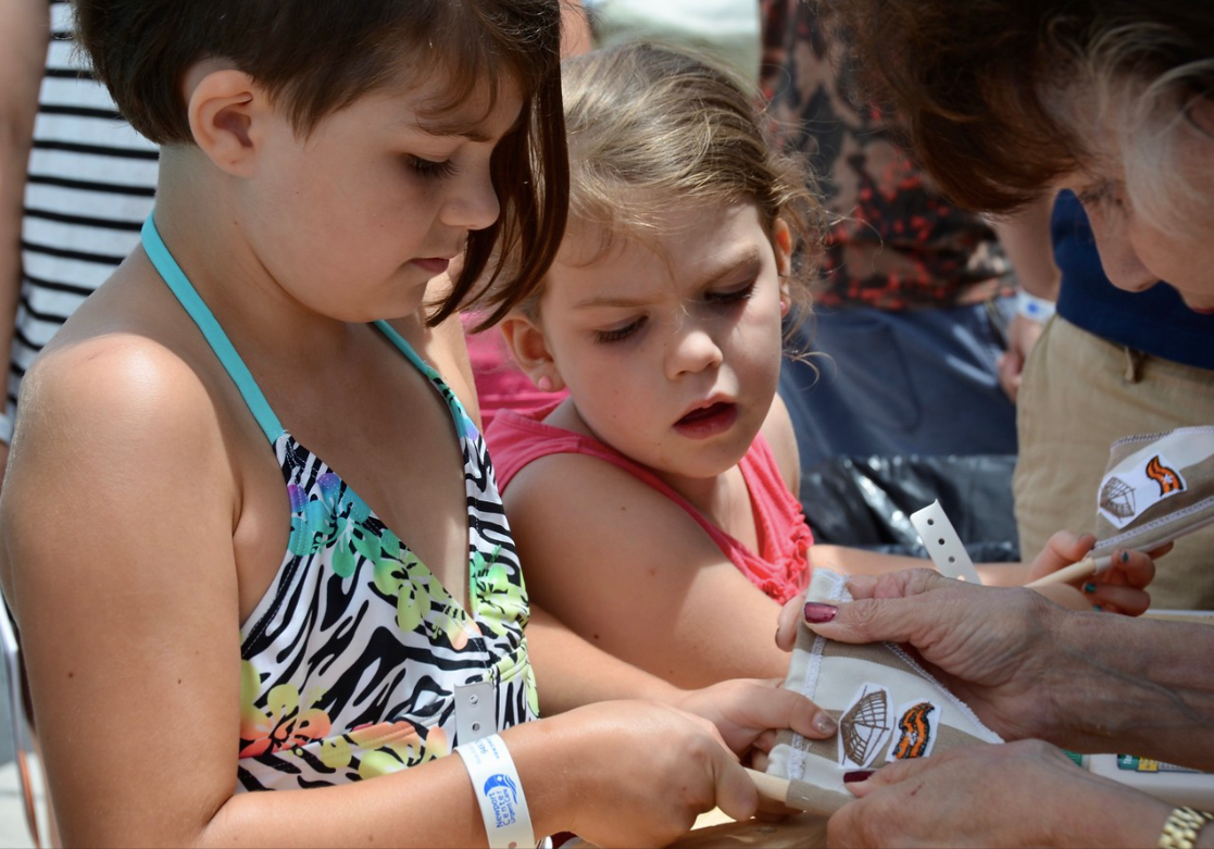 Children opening small packages at an outdoor event, with an adult helping them
