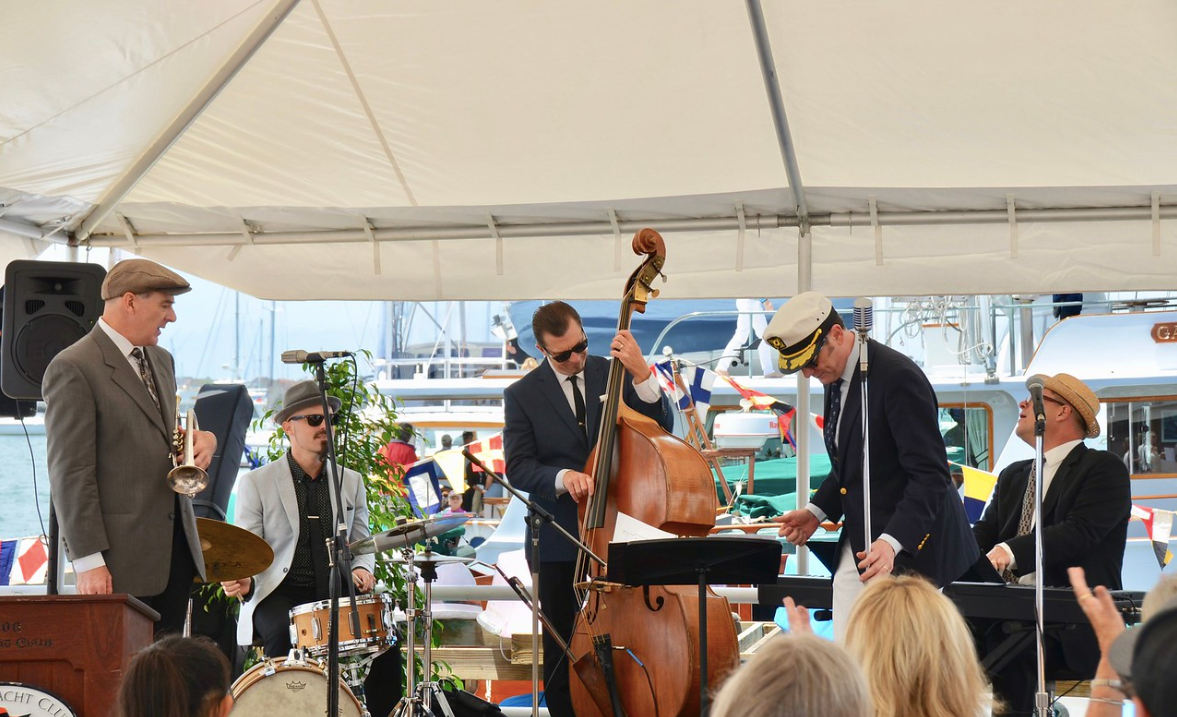 Musicians performing on a tented stage, including a man playing double bass and others with guitars and drums.