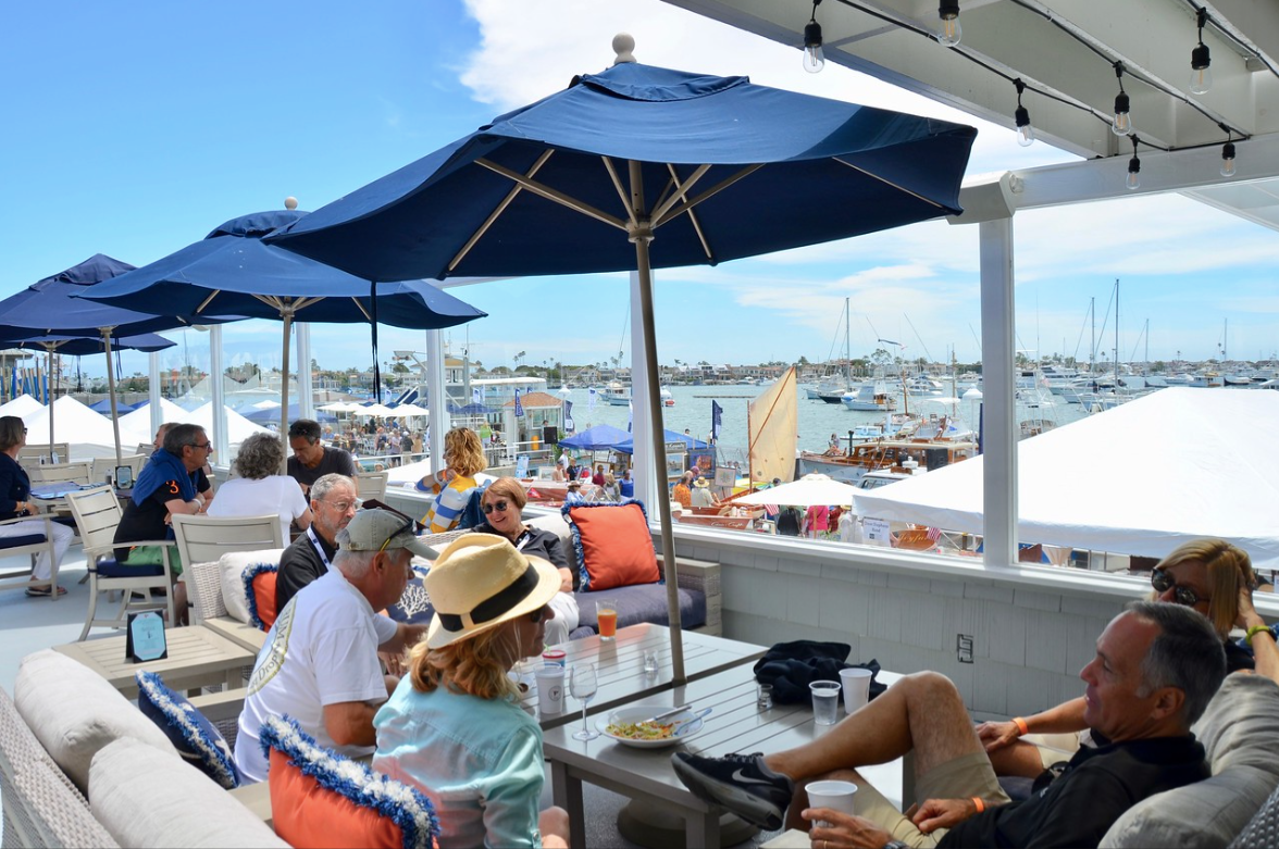 Outdoor waterfront café with blue umbrellas and seated diners overlooking the harbor