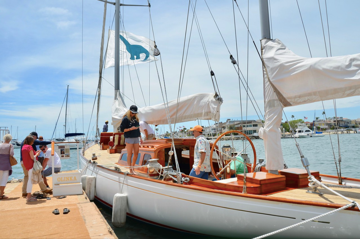 People on a white sailboat docked at a marina on a sunny day