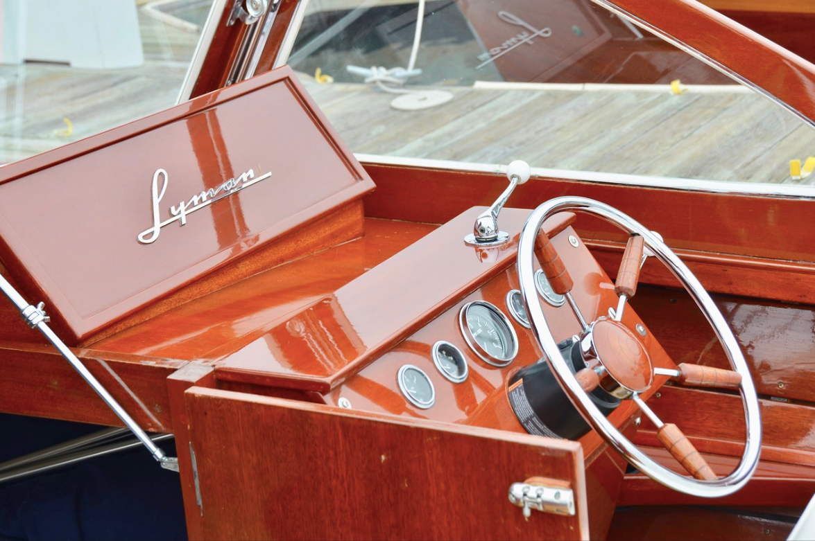 Red boat cockpit with wooden dashboard, white steering wheel, and chrome gauges