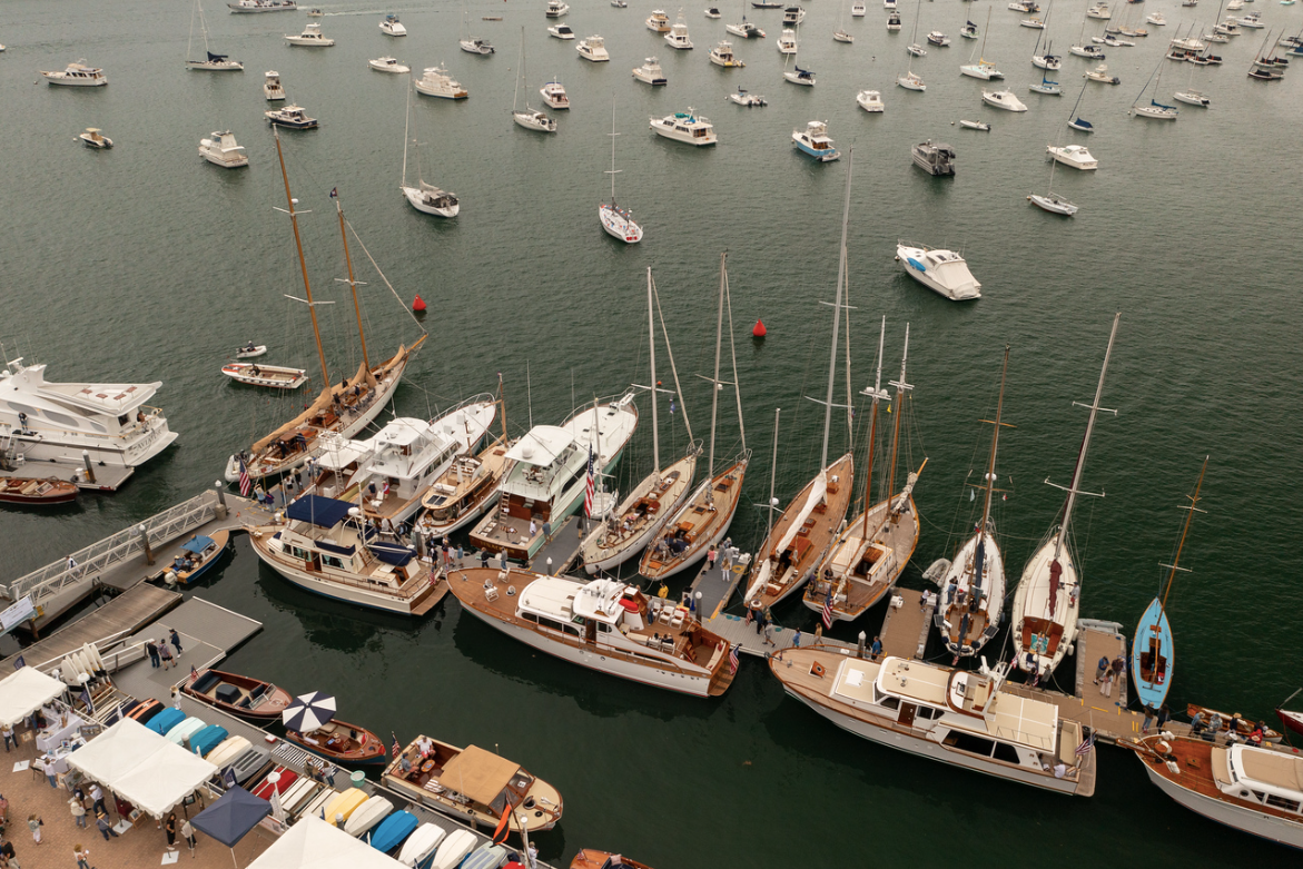 Aerial view of a marina with many sailboats and yachts docked in calm water.