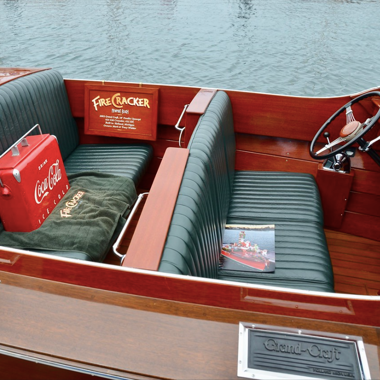 Wooden boat interior with green striped seats, a red cooler, and water outside